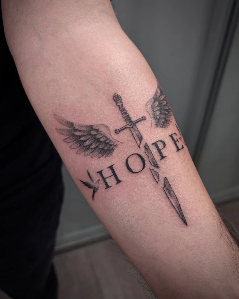 Tatuaj fine line sabie cu aripi HOPE pe antebraț realizat de Sasha la Muntele Tattoo